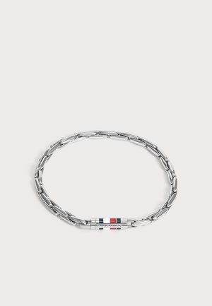 Bracelet chaîne en argent avec des maillons allongés et un fermoir cylindrique présentant des rayures rouges, blanches et bleues sur un fond uni.