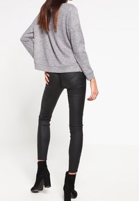 Maglione grigio corto, leggings in finta pelle neri a vita alta e stivali neri alla caviglia. Focus su linee pulite e texture morbide.