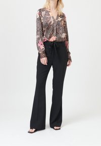 Blouse à manches longues et col en V avec un motif floral et des designs en couleurs foncées rehaussés d'accents roses ; associée à un pantalon noir taille haute avec ceinture.