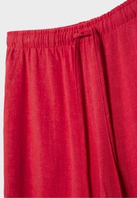 Pantalon avec taille élastique rouge et cordon de serrage, montrant la texture du tissu et les détails de la couture.