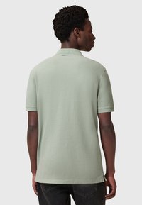 Ljusgrön polo skjorta med korta ärmar, mjukt material, sidoflikar vid fållen och en standardkrage, sedd bakifrån.