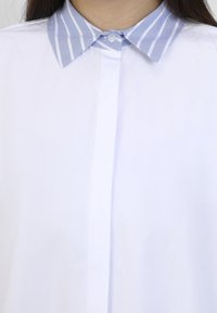 White shirt with a light blue and white striped collar, featuring a buttoned placket and smooth texture. Collar is slightly spread.