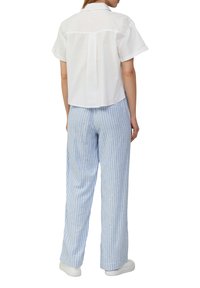 Witte, kortotm shirt met kraag en achterkant met plooien, gecombineerd met lichtblauwe, verticaal gestreepte, wijde broek en witte sneakers.