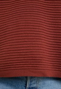 Pull en maille bordeaux côtelée avec une finition texturée, associé à un jean en denim bleu clair, présentant un look décontracté en couches.
