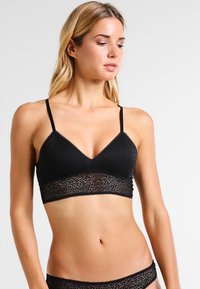 Brassière en dentelle noire avec bretelles réglables, dotée d'un haut texturé et d'une bande en dentelle florale. Matériau doux et extensible avec un design sans couture.