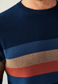 Pull marine à rayures horizontales bleu clair, beige et rouille. Présente un col rond et un tissu doux et texturé.