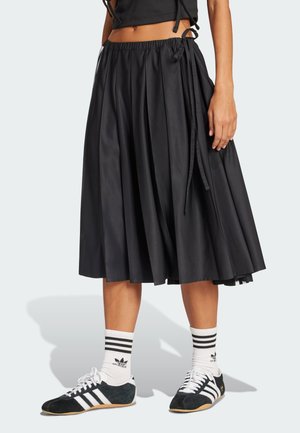 Black pleated skirt with an elastic waistband and side ties; paired with black and white athletic shoes and striped socks.