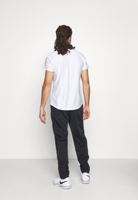 Camisa blanca de manga corta con un patrón de cuadrícula, combinada con pantalones de chándal negros ajustados y zapatillas blancas con detalles negros.