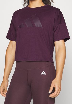 Osoba nosząca ciemnofioletowy skrócony T-shirt Adidas oraz dopasowane legginsy z wysokim stanem, z logo Adidas na obu elementach ubrania.