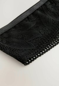 Dentelle noire avec un motif floral, mettant en avant un filet délicat et un bord satin plein, agrémenté de petites découpes régulièrement espacées.