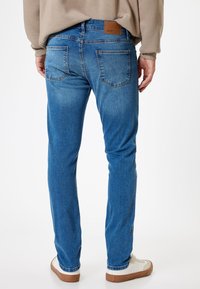 Jeans in denim blu con una vestibilità slim, design a cinque tasche e etichetta in pelle sulla vita. Il tessuto presenta una leggera texture sbiadita.