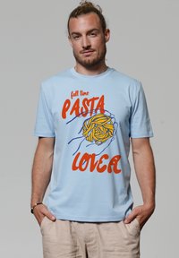 T-shirt en coton bleu clair avec un graphique de pâtes en jaune et bleu. Le texte indique "amoureux des pâtes à temps plein" en lettres rouges en gras.