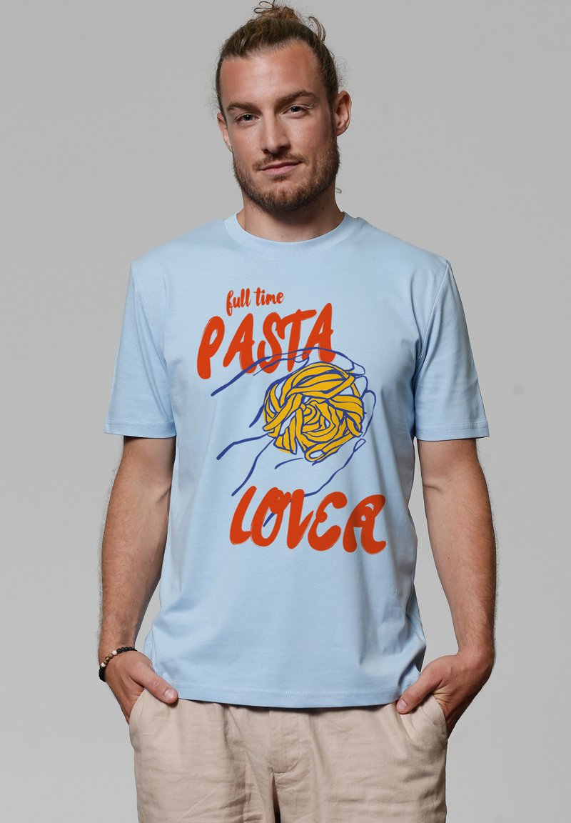 T-shirt en coton bleu clair avec un graphique de pâtes en jaune et bleu. Le texte indique "amoureux des pâtes à temps plein" en lettres rouges en gras.