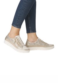 Baskets beige clair avec un motif ondulé texturé en or, dotées de détails à lacets et de fermeture éclair, et d'une épaisse semelle blanche.