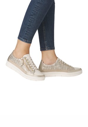 Light beige sneakers with a textured gold wave pattern, featuring lace-up and zipper details, and a thick white sole.