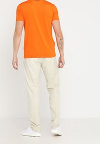 T-shirt orange à manches courtes avec un col rond et un pantalon beige clair. Des baskets blanches complètent la tenue. Design simple sans motifs.