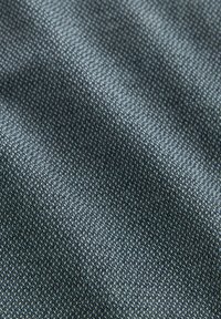 Tissu texturé avec un motif gris foncé, présentant de petits motifs triangulaires dans différentes nuances de gris. Surface lisse et légèrement réfléchissante.