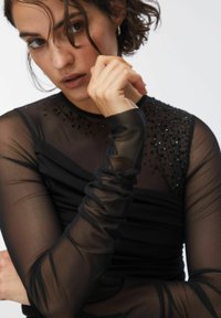 Mustapitsi pitkähihaisen topin, jossa on kerättyjä yksityiskohtia ja koristellut hartiaosan yksityiskohdat. Sileä pinta ja istuva malli.