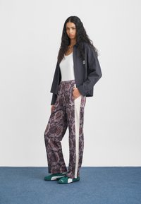 Μαύρο καρό μπουφάν, άσπρη μπλούζα με μανίκια, καρό παντελόνια σε μωβ με κόκκινες και λευκές λεπτομέρειες, και πράσινα PUMA αθλητικά παπούτσια.