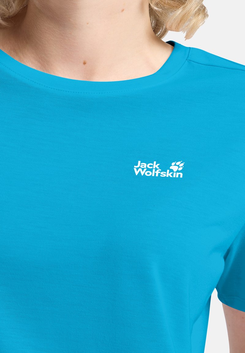 Gros plan sur une personne portant un t-shirt bleu vif Jack Wolfskin montrant le logo sur la poitrine ainsi qu'une partie du cou et de l'épaule.