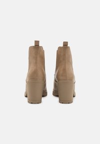 Deux bottines en cuir taupe à finition lisse, avec un talon empilé, des panneaux latéraux élastiques et des languettes arrière pour un enfilage facile.