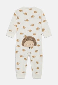 Ein cremefarbener Overall mit Igel-Muster und langen Ärmeln, der auf dem Rücken eine Applikation eines Cartoon-Igels sowie elastische Bündchen an den Ärmeln und Knöcheln aufweist.