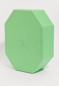 Roheline kaheksanurkne joogatükk, mille ühele küljele on sisse pressitud diskreetne luige logo, seismas ülespoole valgel pinnal.