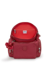 Mochila de tela roja con un zipper redondo, bolsillo interior, parche con logo y un llavero de mono. Textura suave y diseño compacto.