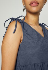 Vestido azul escuro em tecido suave, com decote em V e cintura franzida. Laços ajustáveis nos ombros adicionam detalhe e versatilidade.