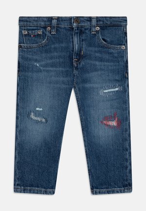 Jeans din denim albastru cu croi drept, prezentând pete uzate și broderie roșie cu pești pe față. Fabricate din material din bumbac.