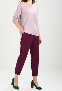 Top de manga larga color lila claro con textura acanalada, combinado con pantalones burdeos de corte cónico y zapatos de tacón alto verde oscuro.