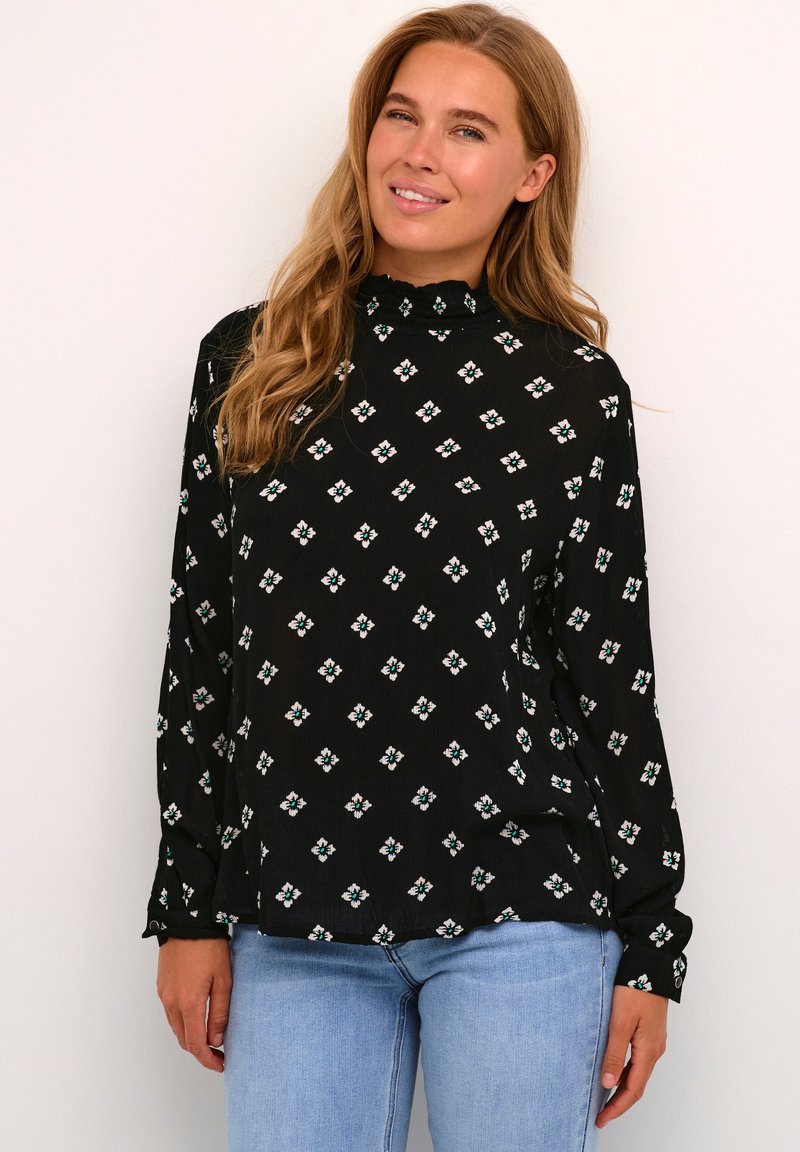 Zwarte blouse met bloemachtige ruitpatronen in wit en groen. Hoge halslijn met een gerimpelde rand, lange mouwen en een losse pasvorm.