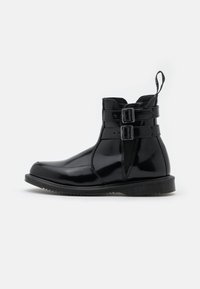 Botas de tobillo de charol negro con dobles hebillas, una textura suave y una suela de goma contrasta con detalle de relieve.