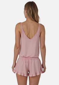 Top rosa sin mangas con un profundo escote en la espalda, combinado con pantalones cortos a juego que tienen un dobladillo con volantes y una cintura elástica. Textura de tela suave.
