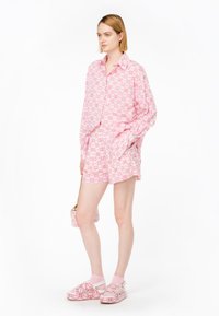Camicia a maniche lunghe rosa con motivo abbinata a pantaloni corti coordinati. Caratterizzata da una vestibilità comoda e una tasca. Sandali rosa spessi e una borsa piccola.
