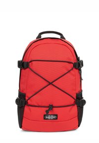 Sac à dos rouge en nylon durable, avec des accents noirs, des sangles latérales réglables, une poignée supérieure et des poches latérales en filet pour un espace de rangement supplémentaire.