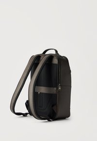 Σκούρα γκρι δερμάτινο σακίδιο με επενδεδυμένη μαύρη πίσω επιφάνεια, διπλούς ιμάντες ώμου και χειρολαβή στην κορυφή, στέκεται όρθιο σε λευκό φόντο.