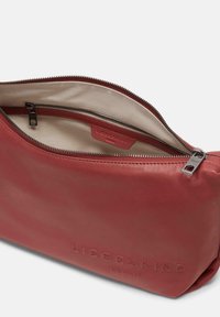 Borsa in pelle rossa con una texture liscia, apertura con zip e foderatura beige. Presenta il nome del marchio impresso sul davanti e accessori in argento.