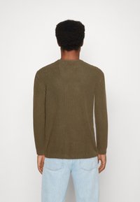 Olivengr�üner Strickpullover mit gerippter Struktur, Rundhalsausschnitt und langen Ärmeln, kombiniert mit hellblauen Jeans.