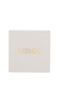 Fyrkantig, mjuk krämfärgad behållare med en slät yta. Ordet "amor" är präglat i guld, centrerat framtill.
