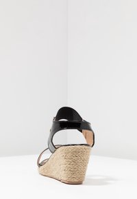 Sandalo con tacco a zeppa in vernice nera, con suola in juta stile espadrillas, apertura sul tallone e cinturino alla caviglia. Suola del tacco testurizzata per una maggiore aderenza.