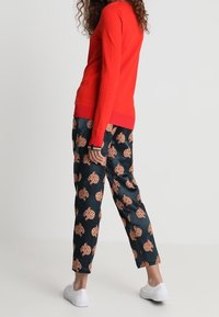 Jersey de punto rojo con puños acanalados, combinado con pantalones azul marino con un estampado repetido en marrón claro. La modelo lleva zapatillas blancas.