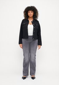 Black denim jacket with button closures, paired with light grey flared pants. Model is wearing a white top and black pointed shoes.