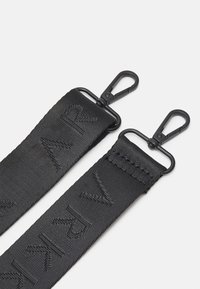 Dwa czarne paski do torby z tkaniny z czarnymi metalowymi obrotowymi hakami na białym tle, jeden pasek wyszywany powtarzającymi się inicjałami marki.