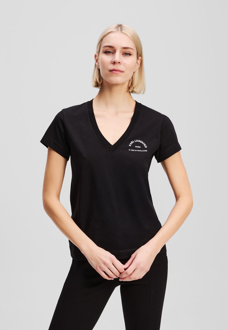 Juodas medvilninis T-shirt su V formos kaklu, trumpomis rankovėmis ir baltu spausdintu tekstu ant krūtinės; paprastas dizainas, laisvas prigludimas, švelni tekstūra.