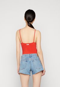 Röd figurnära linne med tunna axelband, parat med ljusblå denimshorts med rå kant och bakfickor. Märkestag synlig på toppen.