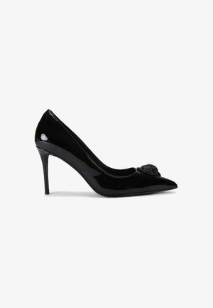 Zwarte gepatenteerde lederen high-heeled pump met een spitse neus, voorzien van een decoratieve versiering aan de voorkant en een slanke stiletto hak.