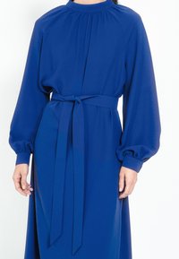 Blaues langärmliges Kleid mit hohem Kragen, gerafften Details an den Schultern, tailliertem Schnitt mit einem passenden Gürtel und weichem, glattem Stoff.