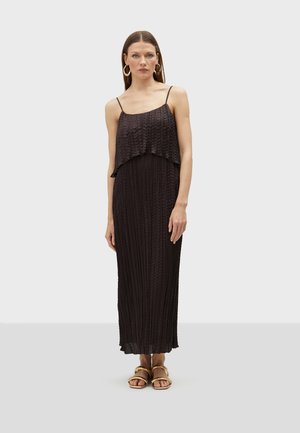 Schwarzes, plissiertes Maxikleid mit gestuften Lagen, verstellbaren Spaghettiträgern und fließender Textur. Kombiniert mit goldfarbenen Sandalen.