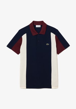 Polo bleu marine avec des panneaux latéraux crème, des manches et un col bordeaux, et un petit logo de crocodile vert sur la poitrine.